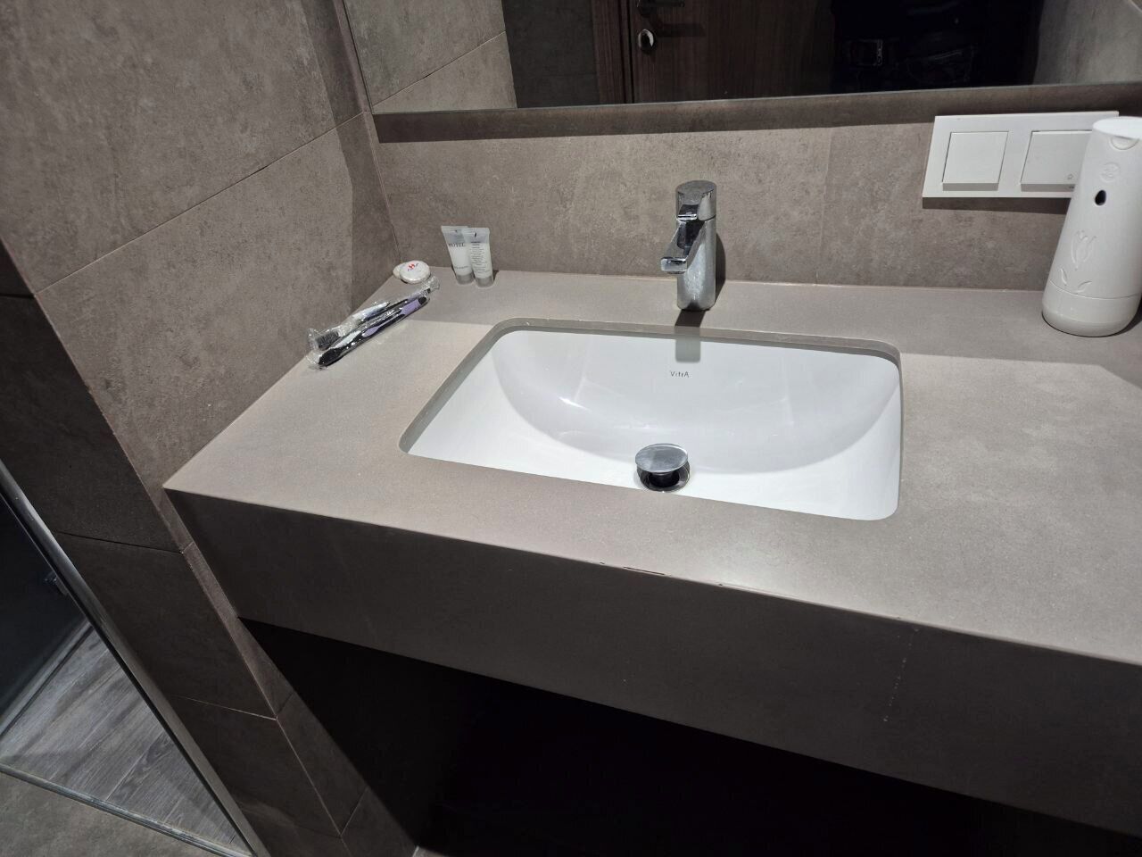 A bathroom with a sink, mirror, and toiletries.