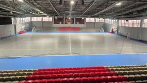 Un gimnasio interior con cancha de baloncesto, zonas de estar y un techo alto con vigas metálicas.