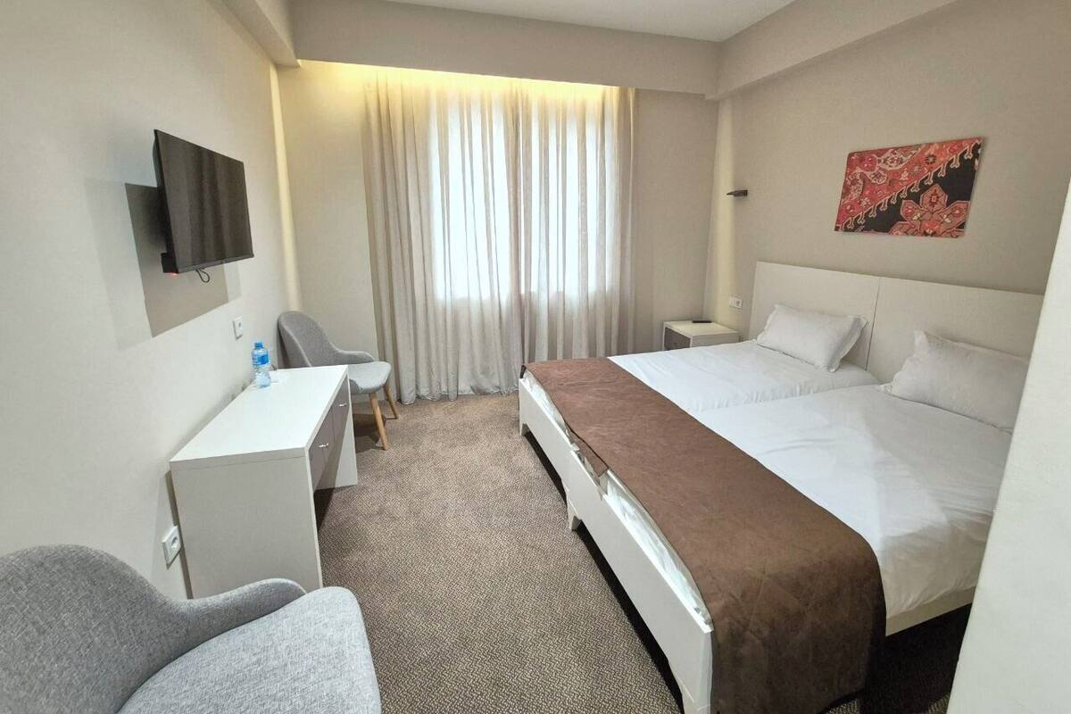 Une chambre d’hôtel équipée d’un lit, d’un bureau, d’une chaise, d’une télévision et d’une fenêtre avec des rideaux.
