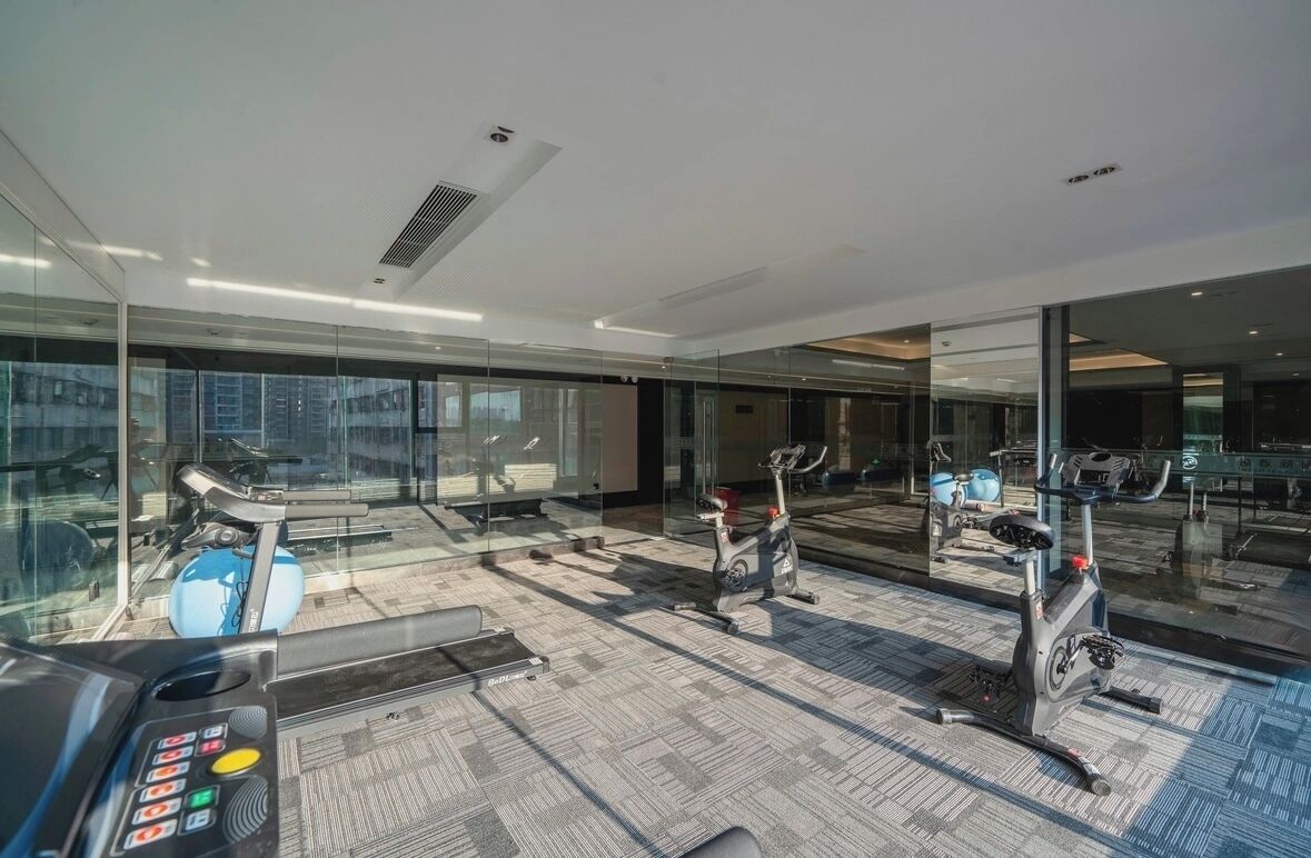 A modern gym with exercise equipment, large windows, and a carpeted floor.
