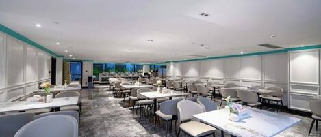 A spacious conference room with multiple tables and chairs, a marble floor, and a view of the outdoors.