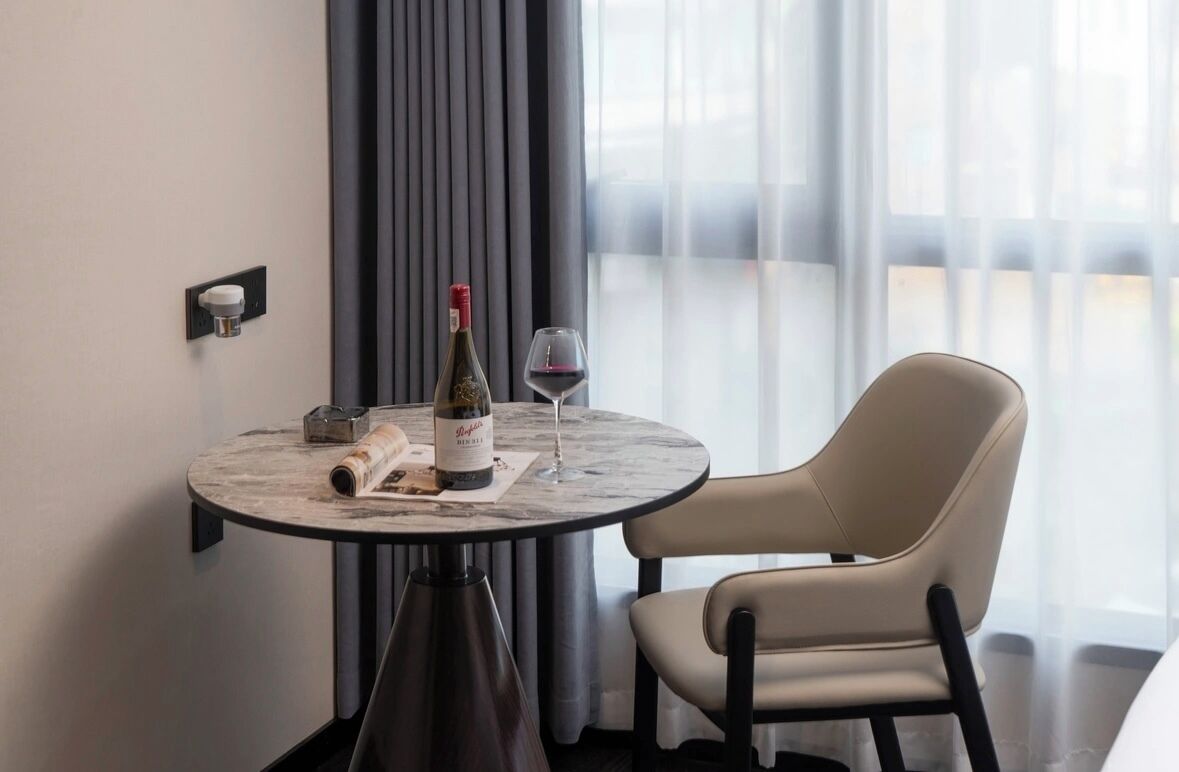 Een ronde tafel met een fles wijn, een glas en een menukaart. Een stoel staat naast de tafel.