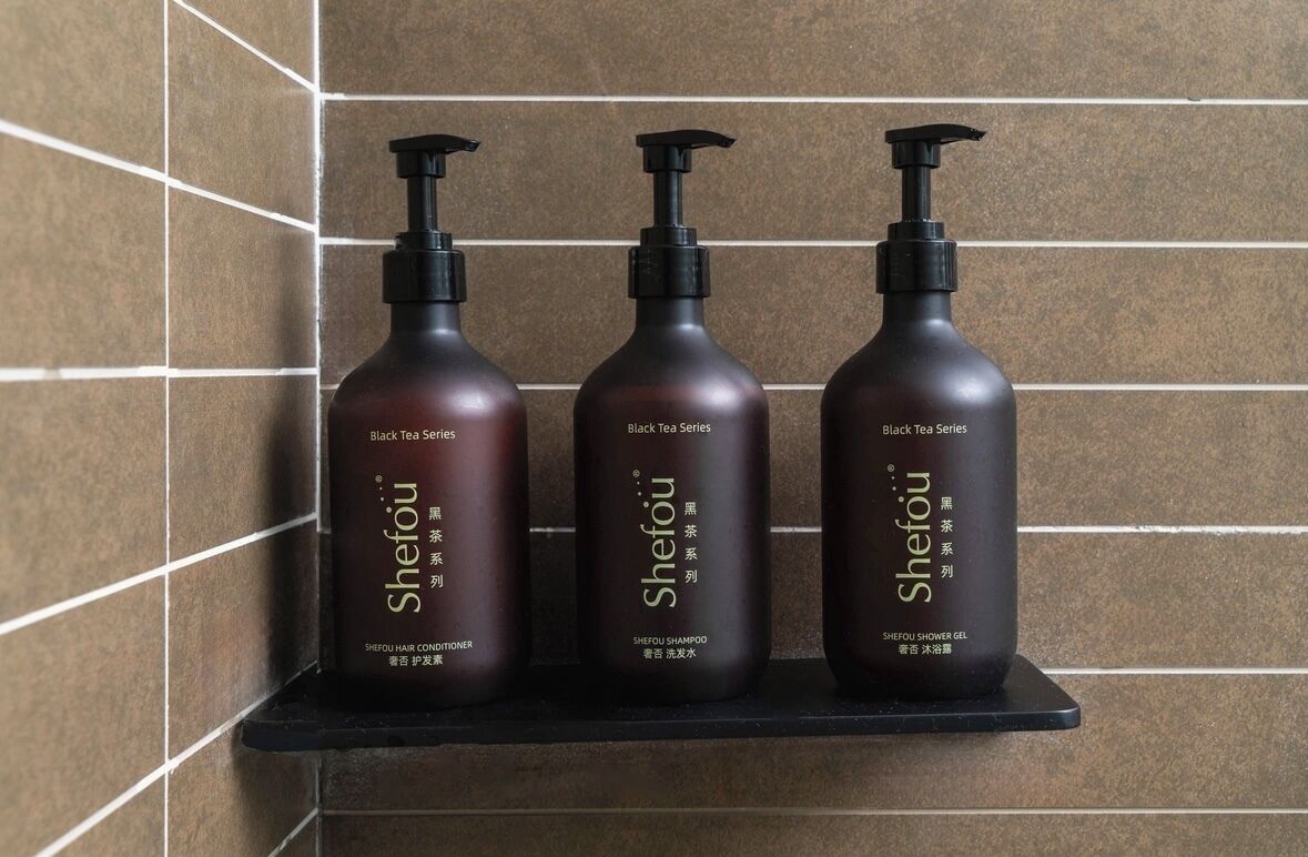 Tres botellas de productos capilares Shefou sobre un estante negro frente a una pared de azulejos.