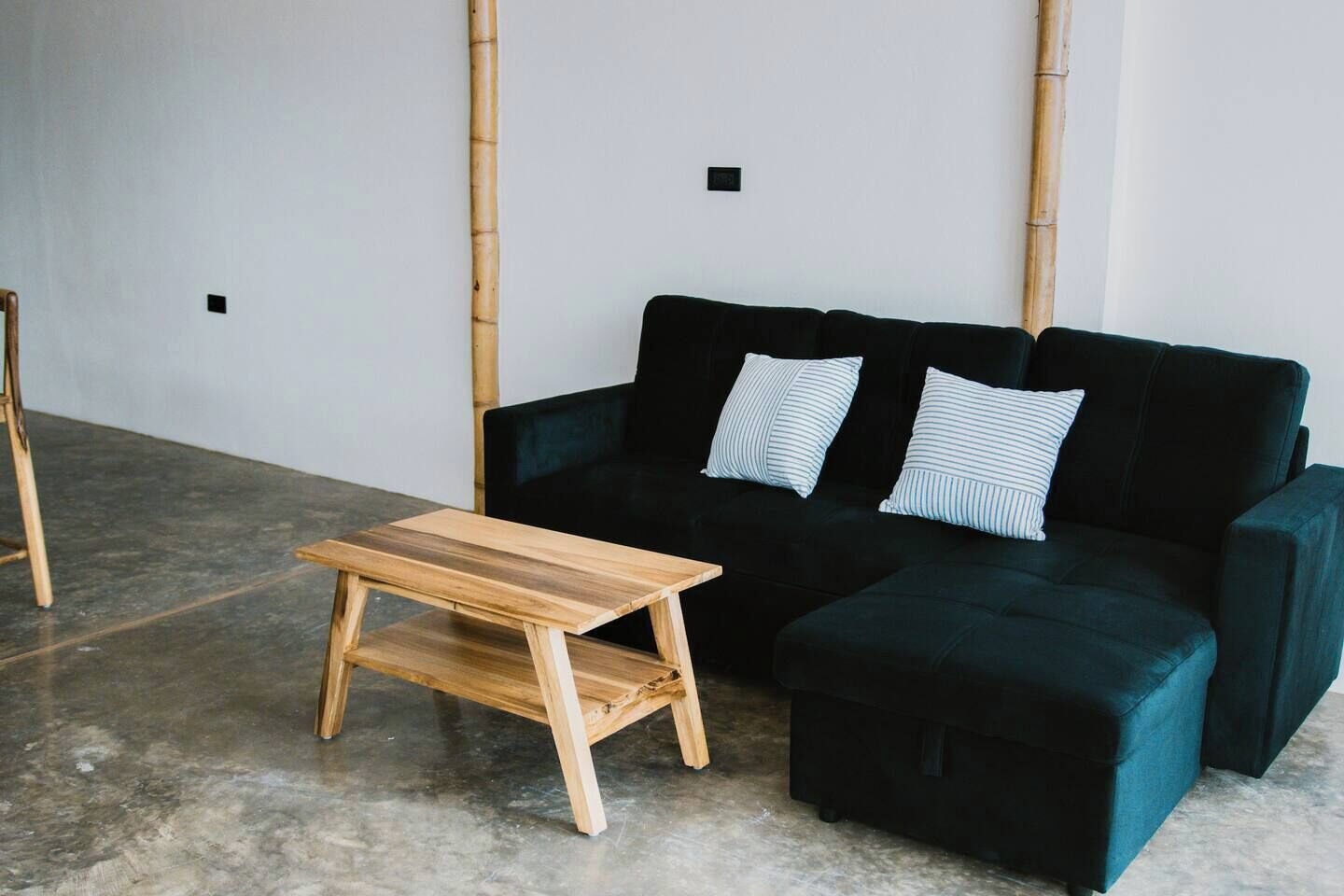 Une pièce avec un canapé vert foncé, deux coussins à rayures et une table en bois.