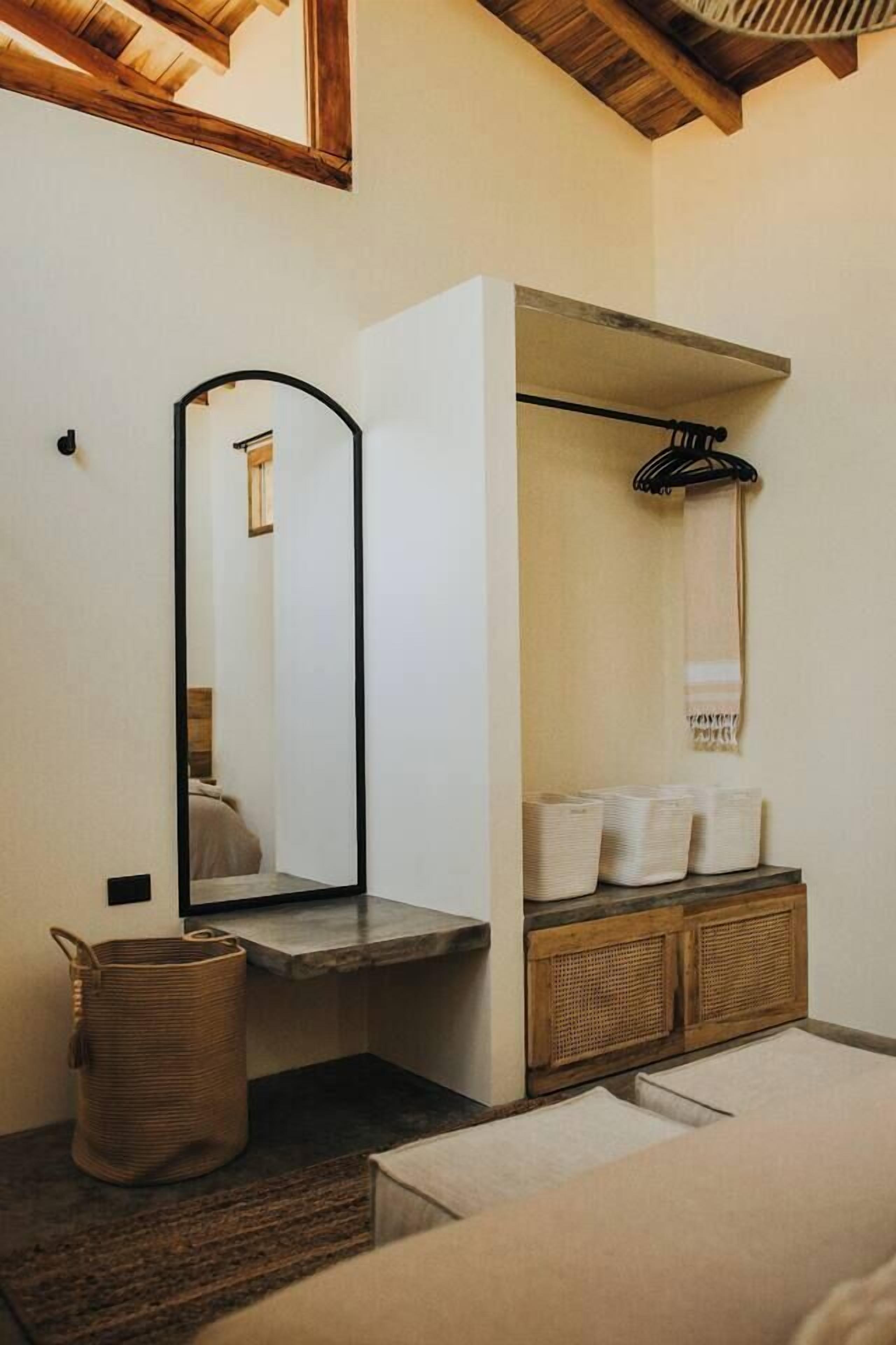 A modern bathroom with a large mirror, a wooden vanity, a towel rack, and a woven basket.