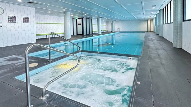 Una piscina interior con agua cristalina, barandales metálicos y suelo de baldosas.