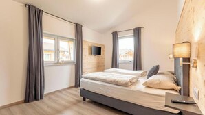 A bedroom with a bed, curtains, a TV, and a lamp. - Chalet 19 with balcony and mountain view (Inzell)