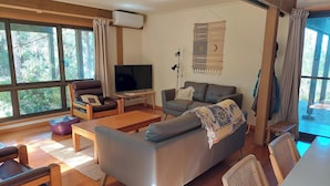Ein Wohnzimmer mit einer Couch, einem Sessel, einem Fernseher und einem großen Fenster.