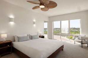 A bedroom with a large bed, bedside lamps, a ceiling fan, and a view of the outdoors through large windows.
