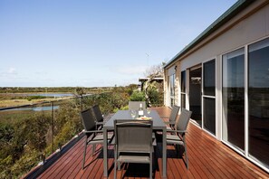 A deck with a table and chairs, overlooking a body of water and a landscape.