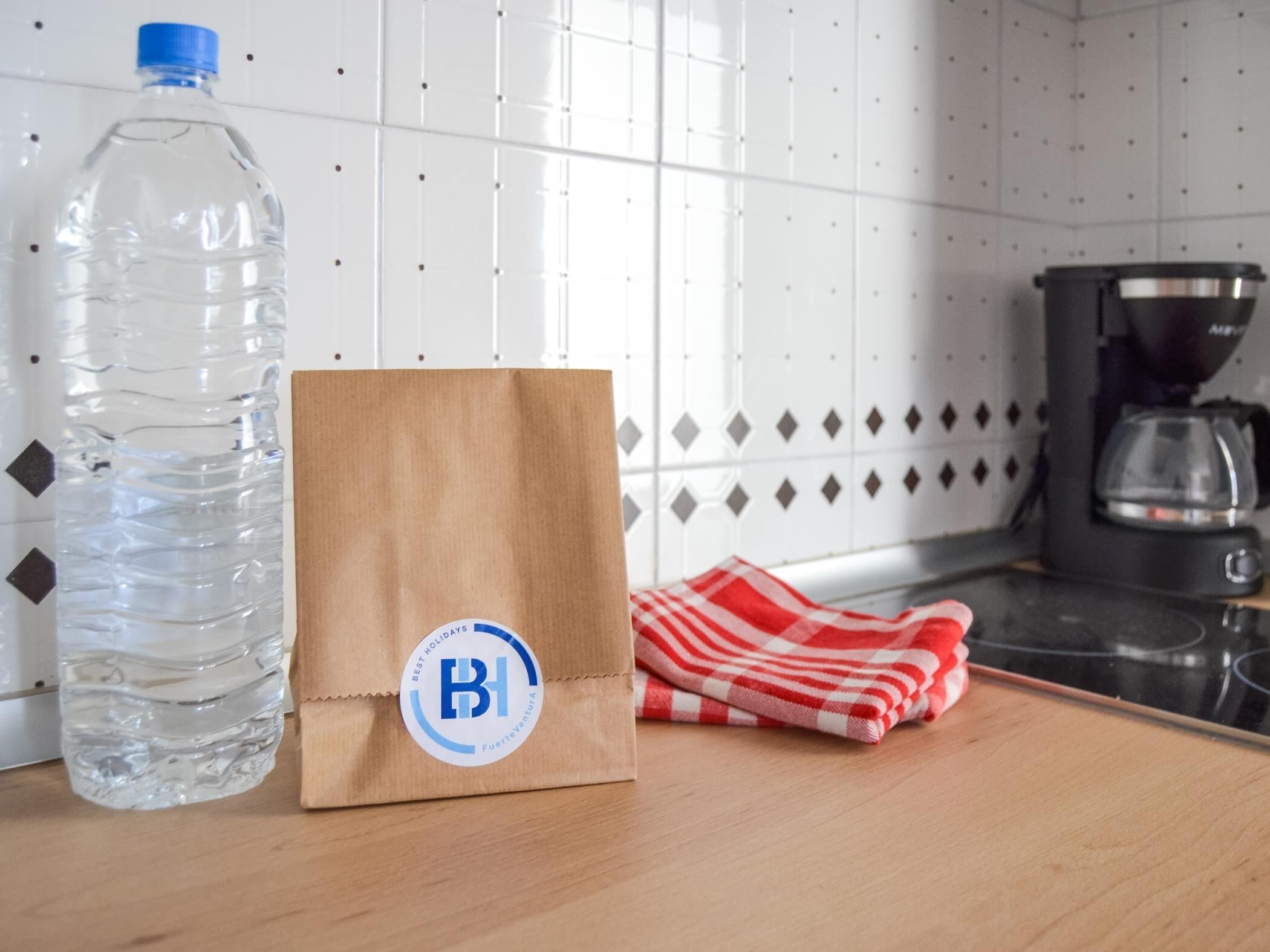 A kitchen counter with a water bottle, a brown paper bag with a logo, and a red and white checkered cloth.