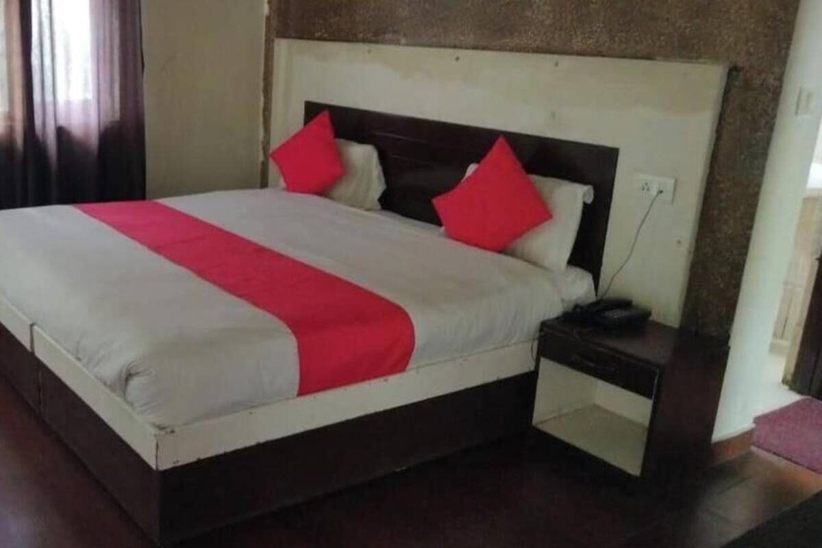 A hotel room with a bed, a nightstand, a small trash bin, and a window with curtains.