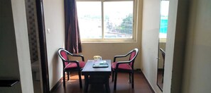 A room with a table and two chairs, a window with a view, and a door leading to another room. - Hotel sparsh ganga (Rishikesh)