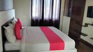 Quarto de hotel com cama, cortinas, televisão e televisão fixada na parede.