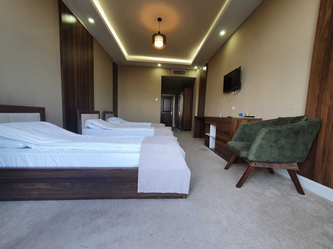Habitación de hotel con tres camas, una silla verde, un televisor de pantalla plana y un escritorio de madera.