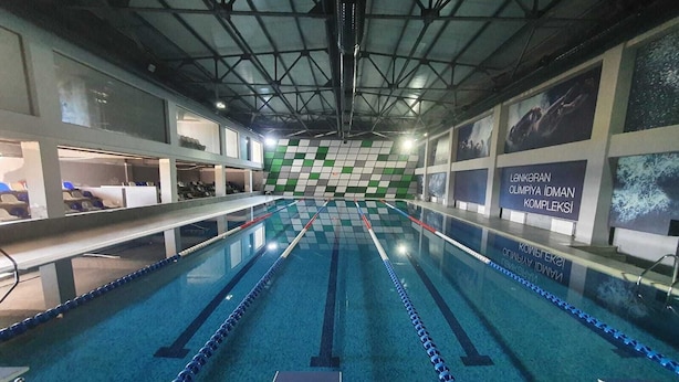 An indoor swimming pool with lanes, a tiled wall with a green and white pattern, and a sign in Turkish.