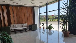 A spacious lobby with a modern design, featuring a sofa, a coffee table, and several potted plants.