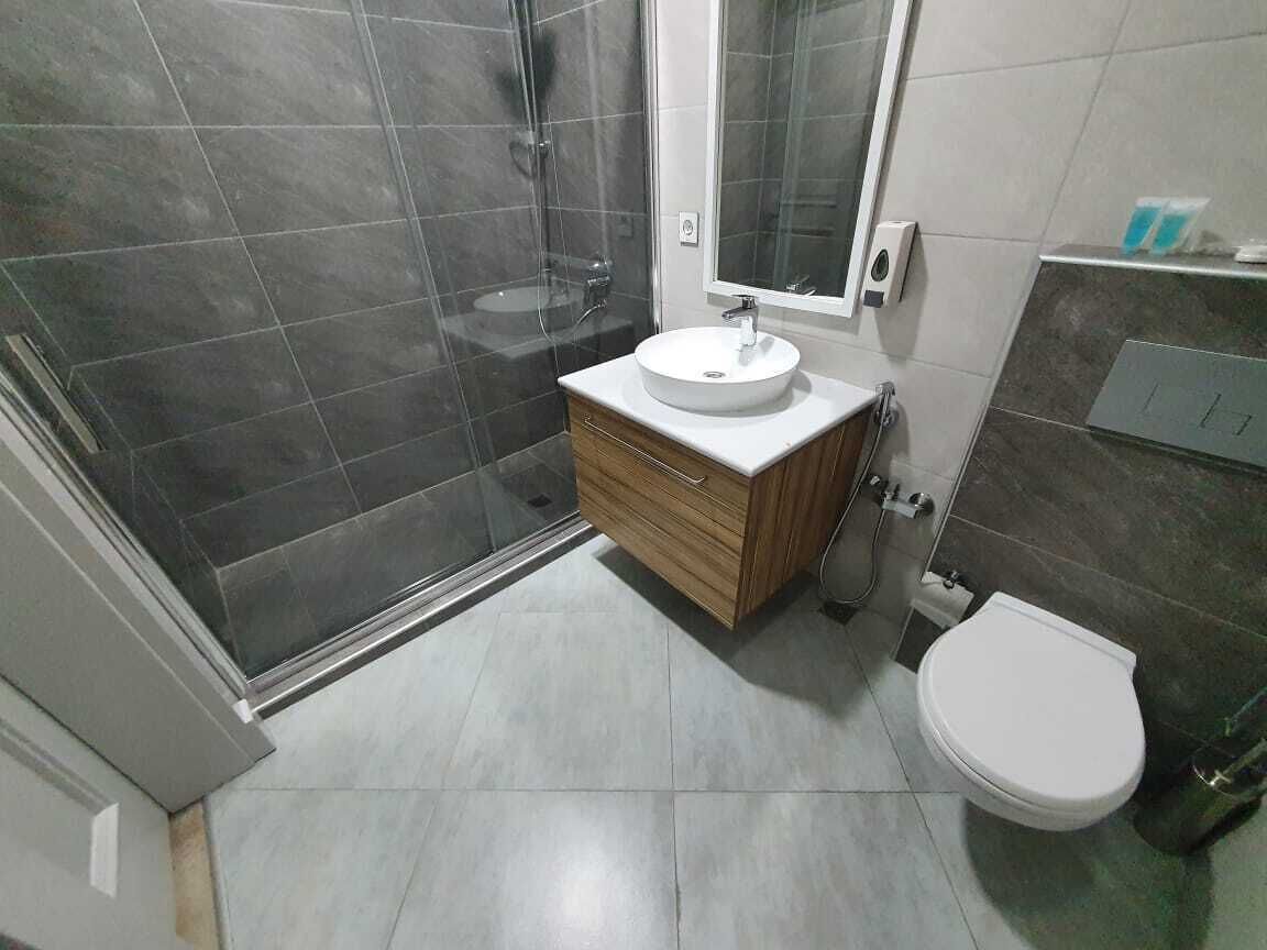 Un bany modern amb un box de dutxa de vidre, un lavabo blanc amb un moble de tocador de fusta i un vàter.