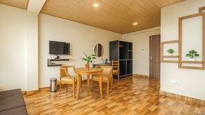 A room with a wooden floor, a dining table with chairs, a TV mounted on the wall, a bookshelf, and a door leading to another room. - TVD Hotel Polaris Near Mg Marg (Gangtok)