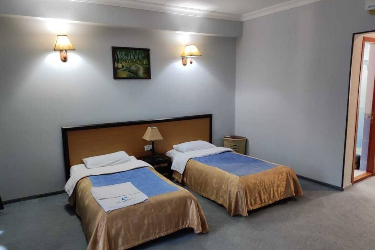 Une chambre d’hôtel avec deux lits, une tête de lit en bois, des lampes de chevet, une petite table et un tableau au mur.