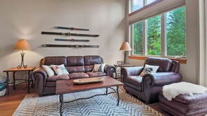 A living room with a leather sofa, armchair, and coffee table, a rug, and skis mounted on the wall.