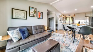 Een moderne woonkamer met een leren bank, een eettafel met stoelen, en een keuken in de achtergrond.