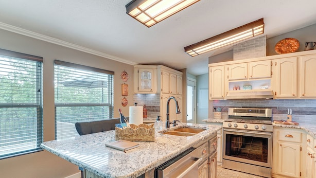 A kitchen with a granite countertop, stainless steel appliances, and light-colored cabinetry. - Outdoor Kitchen + Hot Tub: Table Rock Lake House (Golden)