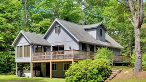 Une maison à deux étages avec un balcon, entourée d’arbres.