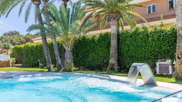 A swimming pool with a waterfall feature, surrounded by palm trees and a hedge. - Moraira Club 210 - Grupo Turis - Moraira, Costa Blanca (Moraira)