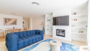 A modern living room with a sectional sofa, a fireplace, a TV mounted on the wall, and a dining area with a table and chairs. - Moraira Club 210 - Grupo Turis - Moraira, Costa Blanca (Moraira)