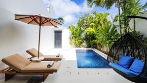 A modern outdoor pool area with lounge chairs and a hanging chair, surrounded by lush greenery. - Villa Gael by Pertama Stay (Seminyak)