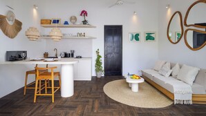A modern kitchen with wooden flooring, a dining area with a wooden table and chairs, a living room with a sofa and a coffee table, and a dark wooden door. - Villa Gael by Pertama Stay (Seminyak)