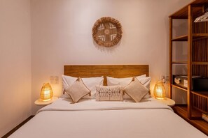 A neatly made bed with a wooden headboard, two bedside lamps, and a wall-mounted decorative item. - Villa Gael by Pertama Stay (Seminyak)
