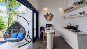 A modern kitchen with a hanging chair, a dining table, and a kitchen island. - Villa Gael by Pertama Stay (Seminyak)