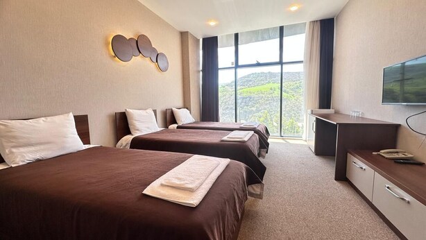 A hotel room with two beds, a desk, a TV, and a large window with a view of hills. - Arena Hotel Yardimli (Yardimli)