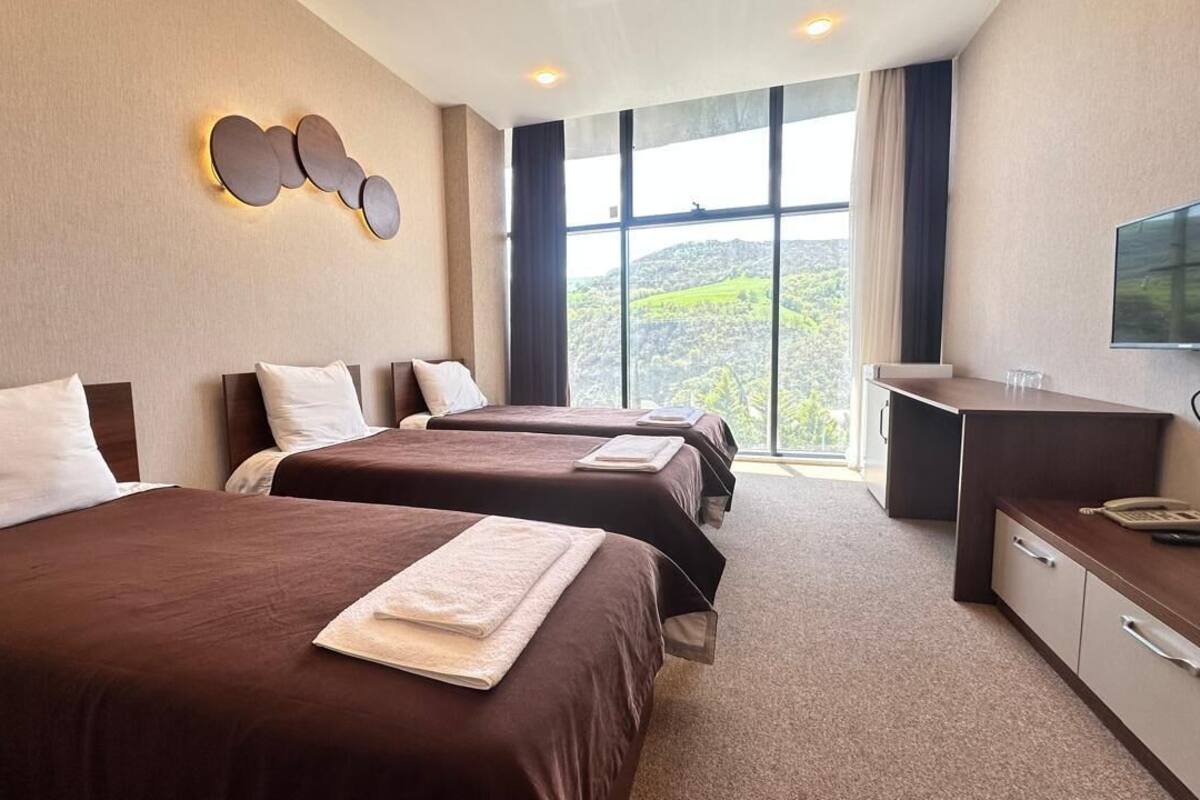 Ett hotellrum med två sängar, ett skrivbord, en TV och ett stort fönster med utsikt över kullar.