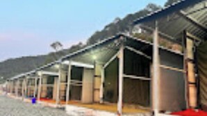 A row of single-story buildings with open sides, likely a campground or caravan park. - Veda Cottage (Barkot)