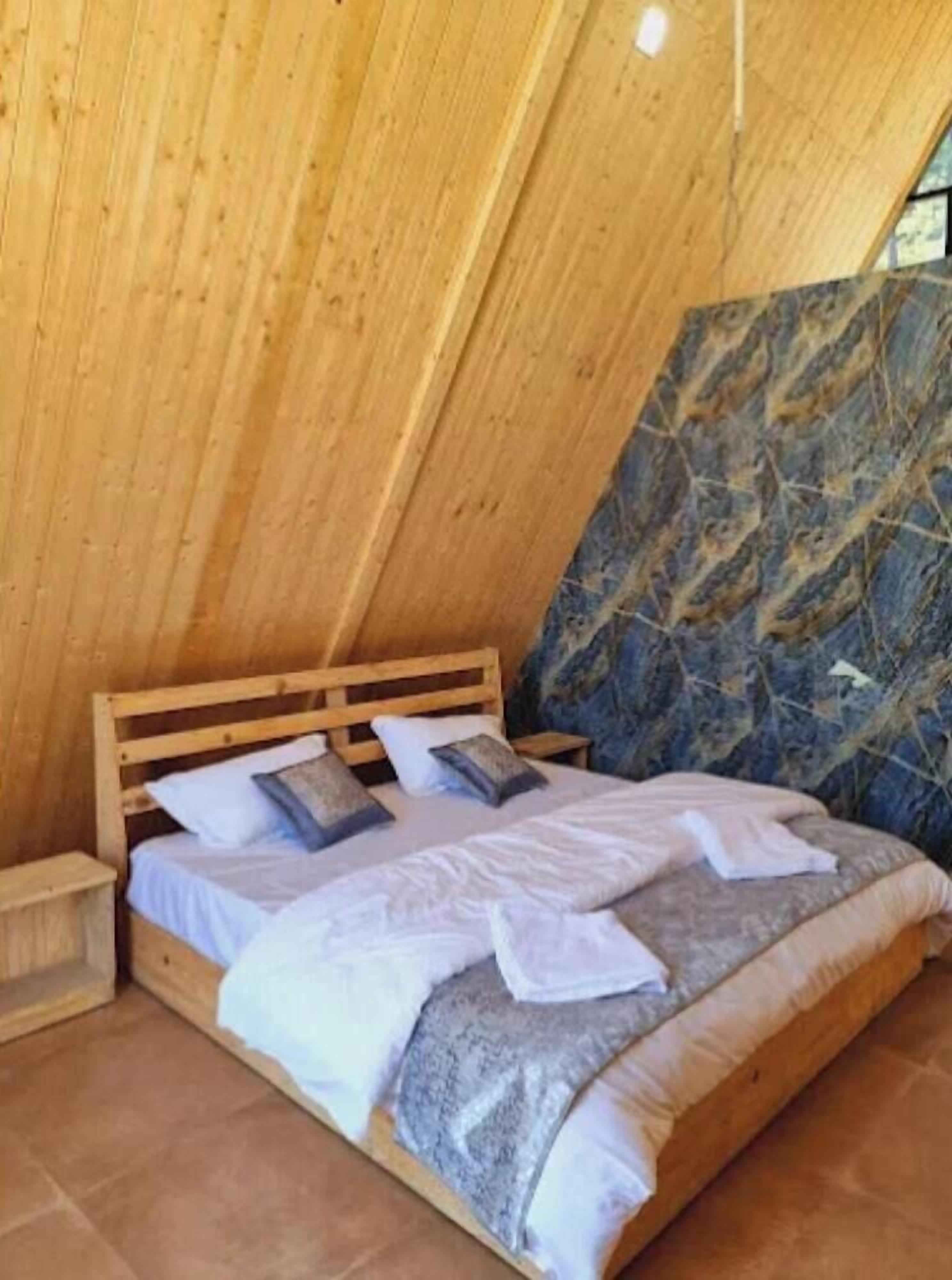 A bedroom with a wooden sloped ceiling, a bed with white bedding, and a blue patterned wall.
