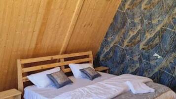 A bedroom with a wooden sloped ceiling, a bed with white bedding, and a blue patterned wall.