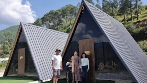 A modern, triangular-roofed building with a grassy entrance area and a gravel path leading to it. - Veda Cottage (Barkot)