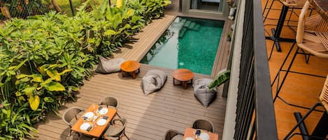 A rooftop pool area with wooden decking, seating, and a small table set for dining.