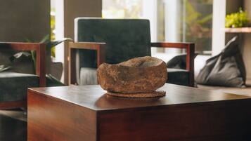 A rustic stone bowl on a wooden table in a modern living room with green chairs and a large window.