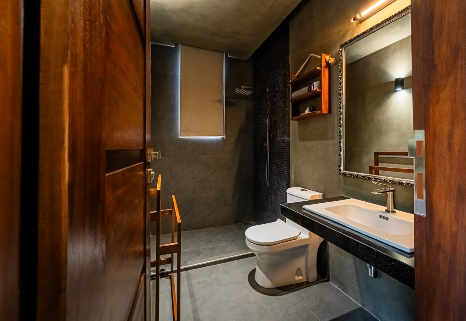 Un baño moderno con puerta de madera, inodoro, lavamanos y ducha.