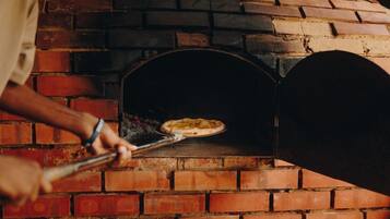Una persona usando una pala para pizza para introducirla en un horno de ladrillo.
