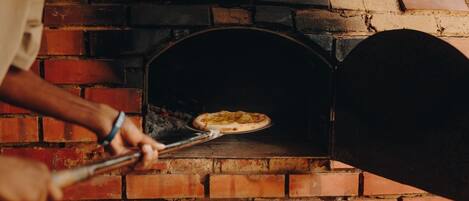 Una persona usando una pala para pizza para introducirla en un horno de ladrillo.