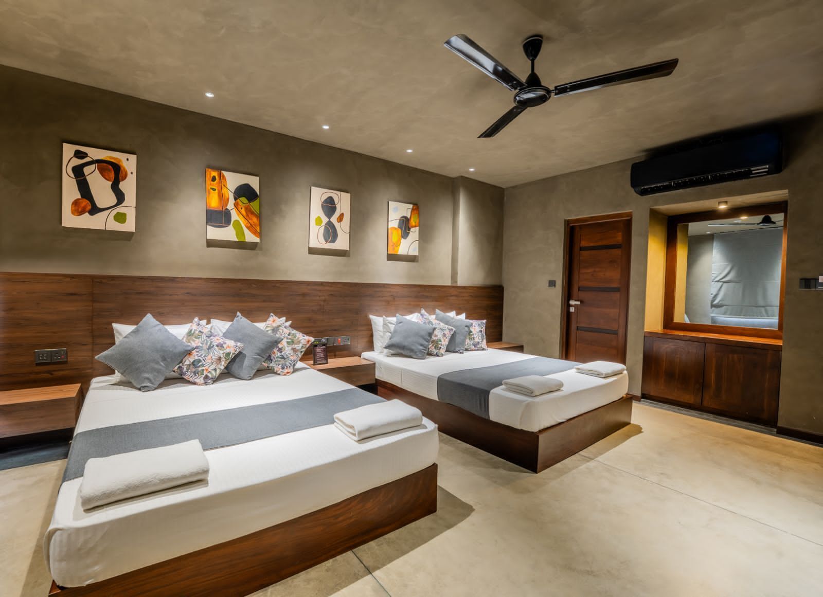 A modern hotel room with two beds, a ceiling fan, artwork on the walls, and a window with curtains.