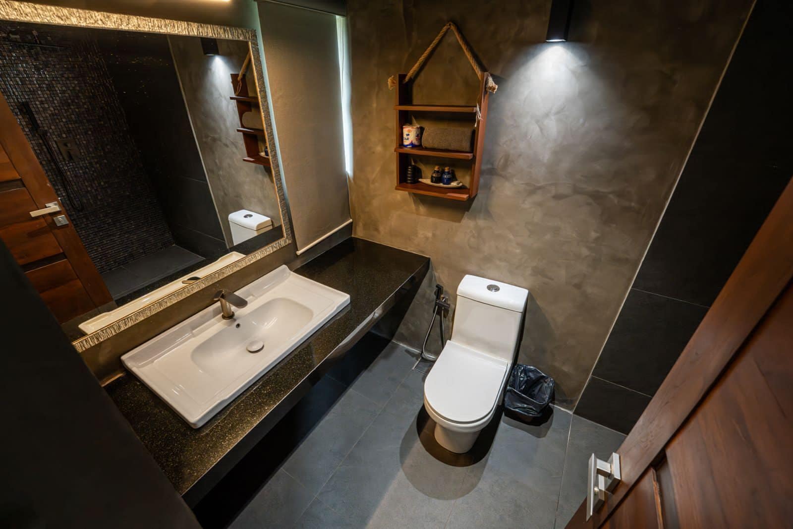 Ein modernes Badezimmer mit einem großen Waschbecken, Toilette und einem hölzernen Ablagebrett für Toilettenartikel.