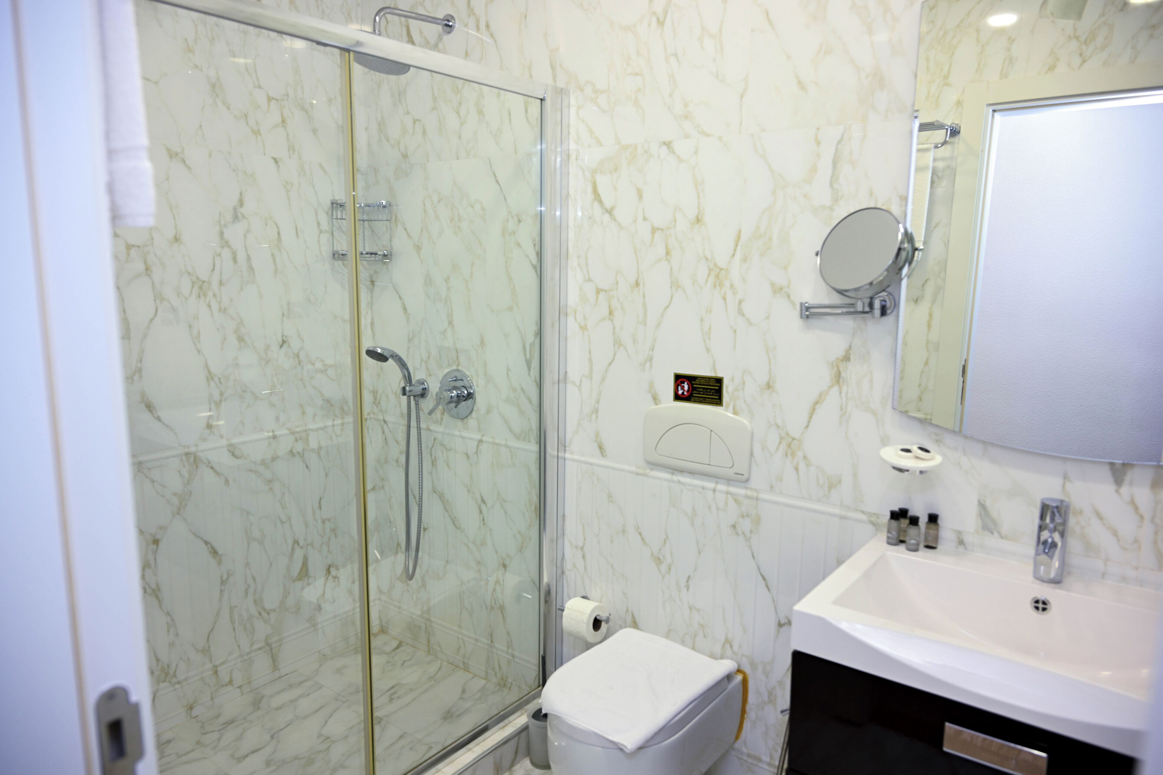 Un baño moderno con ducha de vidrio, un lavamanos blanco y pared con azulejos de mármol.