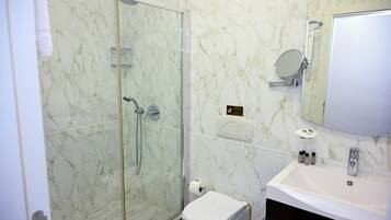 Un baño moderno con ducha de vidrio, un lavamanos blanco y pared con azulejos de mármol.