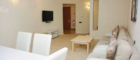 Una sala de estar moderna con un sofá, una mesa de comedor y sillas. Hay un televisor de pantalla plana montado en la pared.